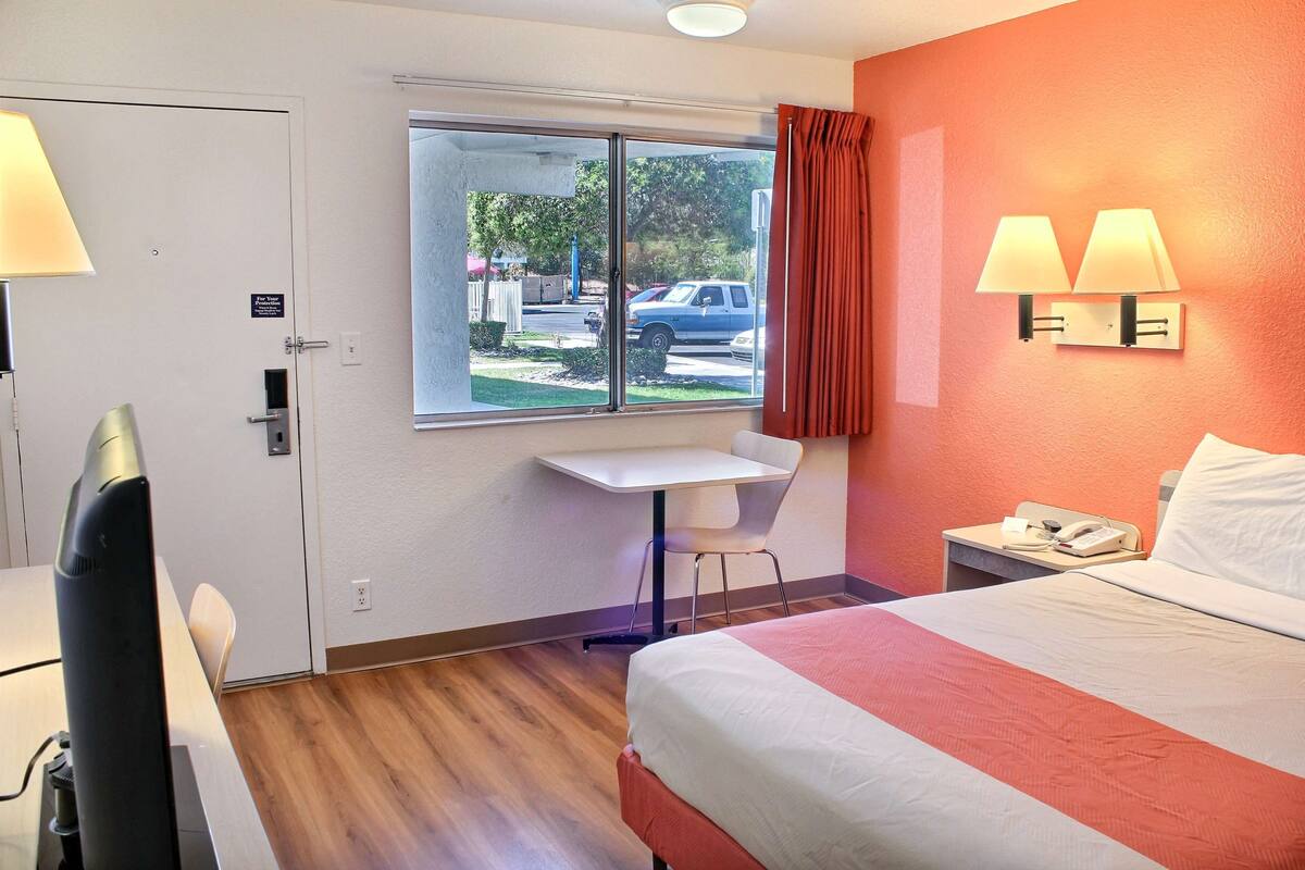 Quarto de hotel com cama, escrivaninha e janela com vista para o exterior.