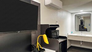 A hotel room with a flat-screen TV, a microwave, a sink with a mirror, and a yellow lamp. - Motel 6 Atascadero, CA (Atascadero)