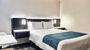 A hotel room with a bed, a bedside table, a chair, and a desk.