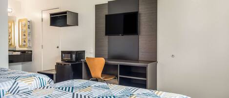 Quarto de hotel com duas camas, televisão presa na parede, uma escrivaninha com cadeira e micro-ondas.