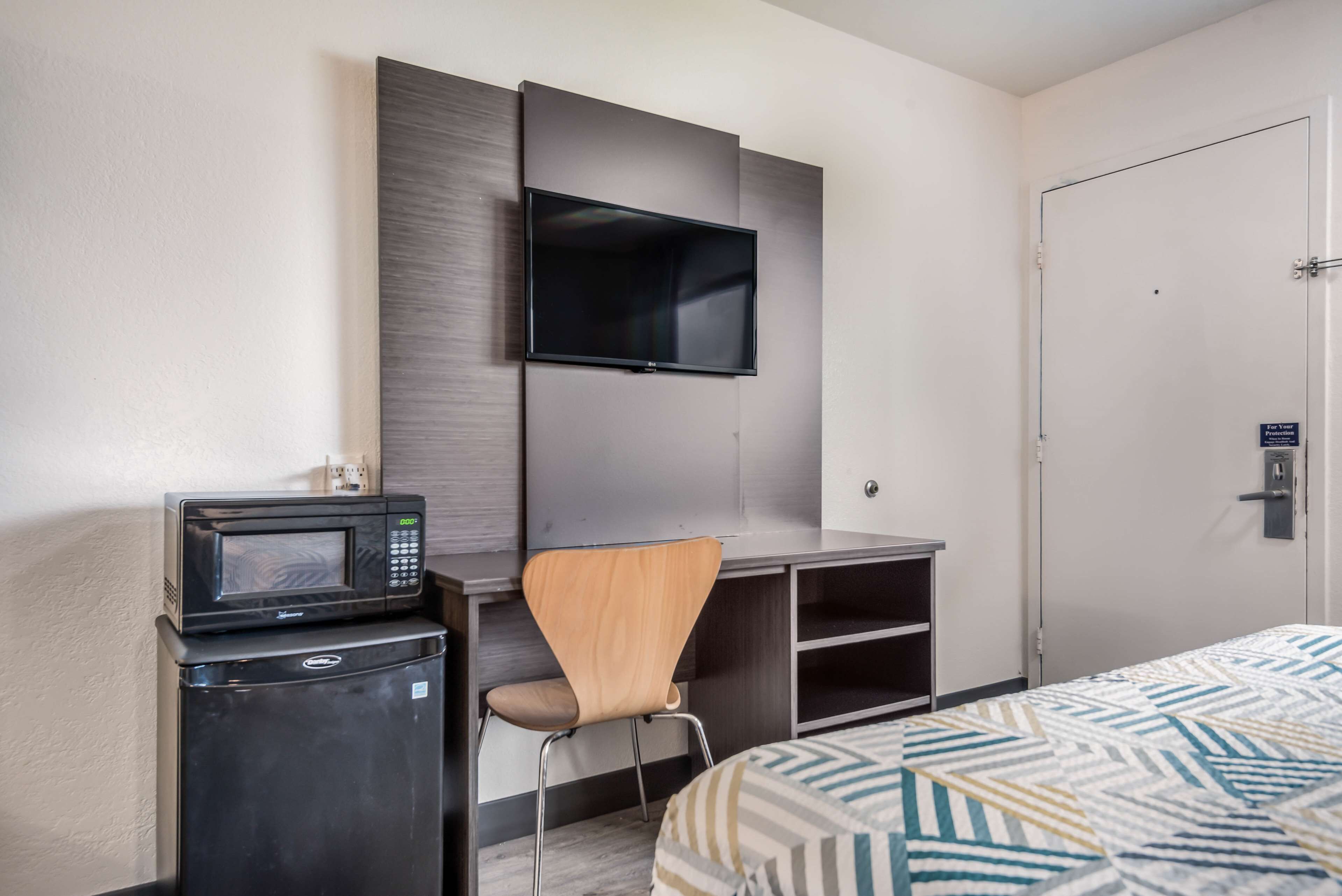 A hotel room with a bed, a TV mounted on the wall, a microwave, and a small refrigerator.