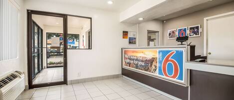 A hotel reception area with a large number '6' sign, a reception desk, and a view of the outside through a glass door.