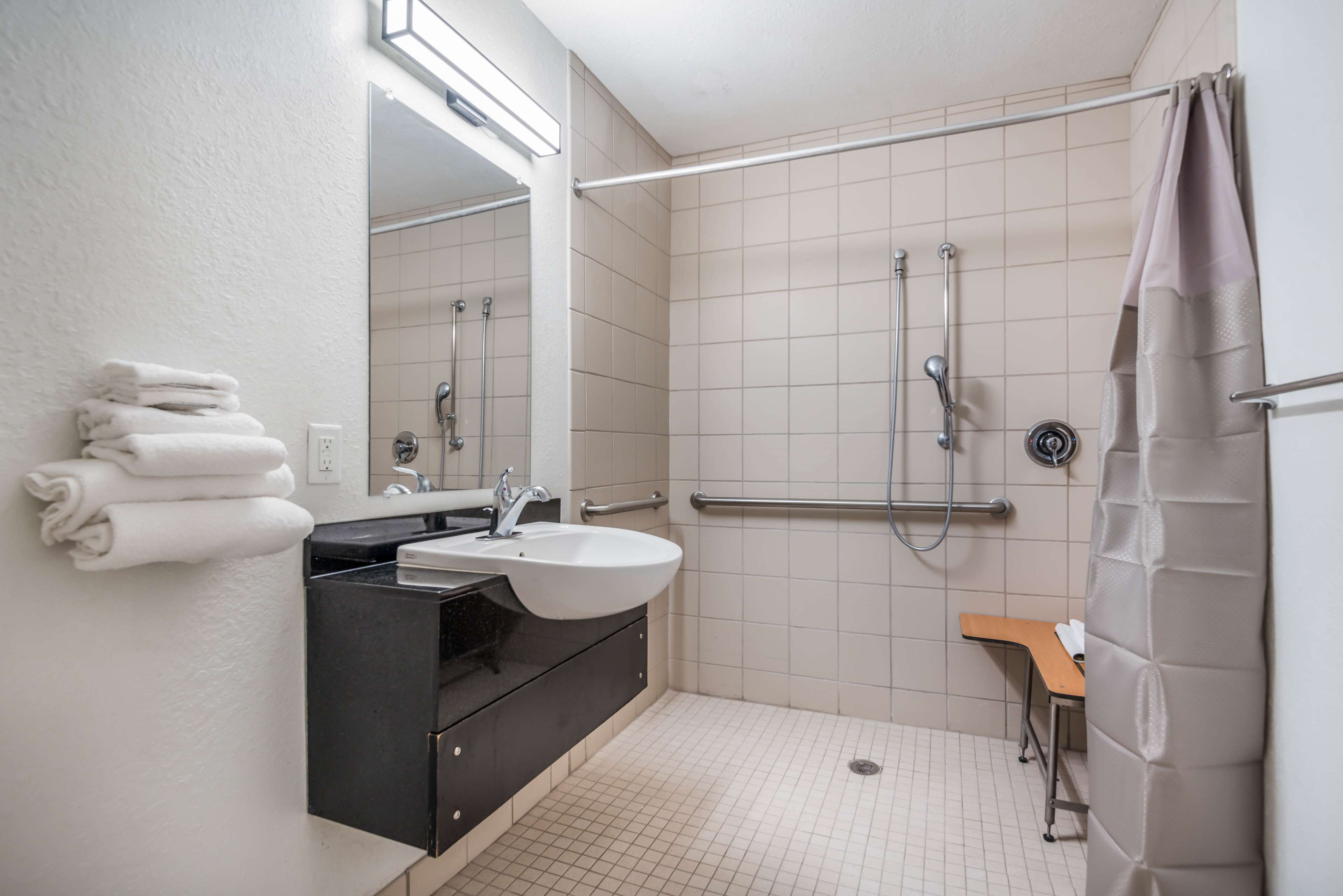A bathroom with a sink, mirror, and a shower area with a grab bar.