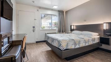 A modern hotel room with a bed, a desk, a flat-screen TV, and a window with curtains.