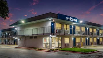 A motel with a 'Welcome' sign, multiple rooms, and a parking lot.