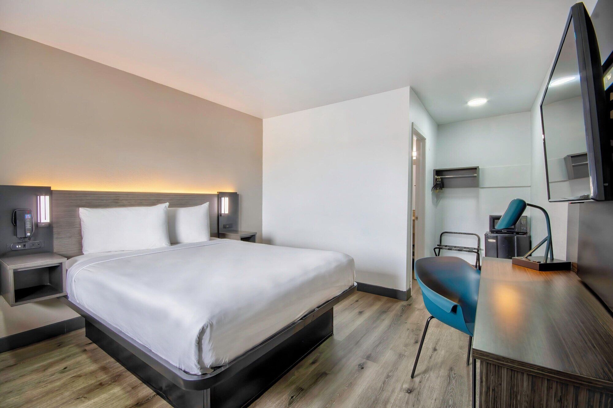 A hotel room with a bed, bedside table, lamp, and a desk with a chair.