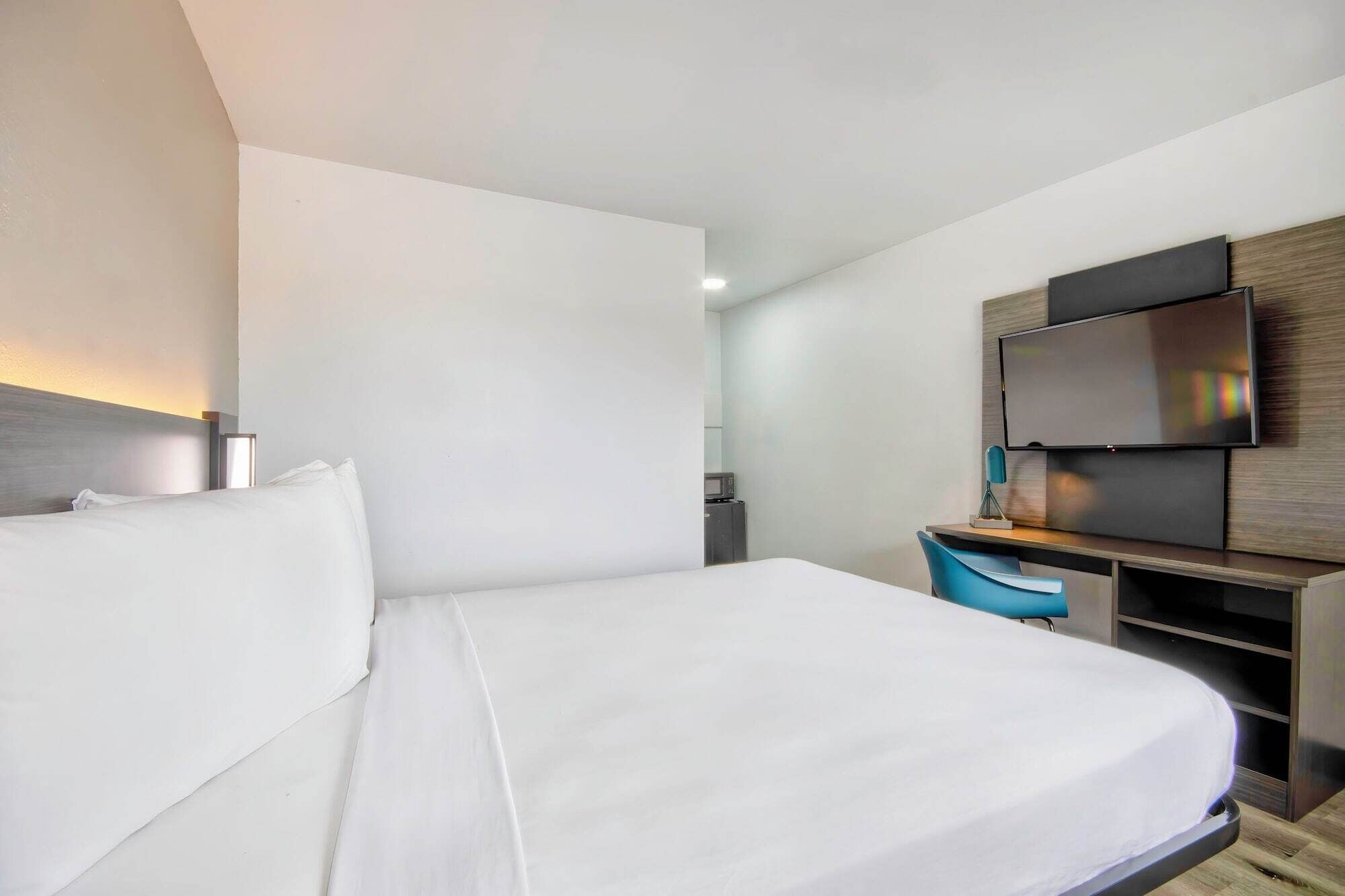 A modern hotel room with a large bed, a desk with a chair, a flat-screen TV, and a microwave in the corner.