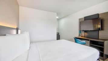 A modern hotel room with a large bed, a desk with a chair, a flat-screen TV, and a microwave in the corner.