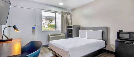 Una habitación de hotel con cama, escritorio, silla y un microondas.