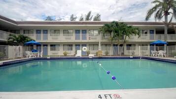 A swimming pool with a 4 FT depth marker, surrounded by a white fence, and a building with balconies and windows in the background.