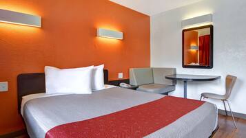 Een hotelkamer met een bed, een bureau, een stoel, een klein tafeltje en een spiegel.