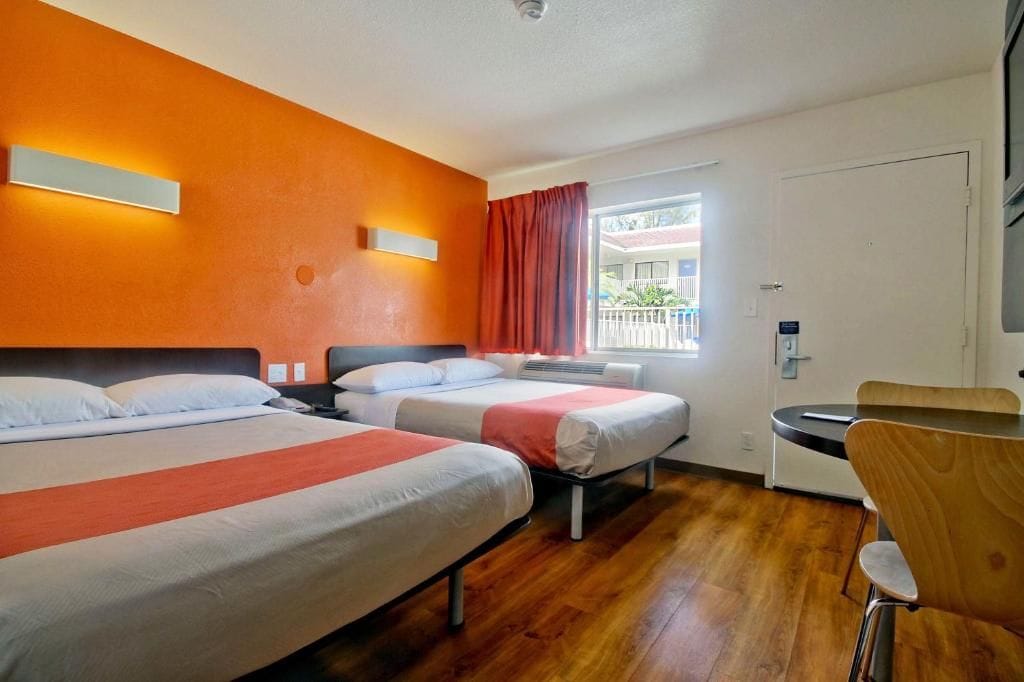 Quarto de hotel com duas camas, uma escrivaninha e uma cadeira.