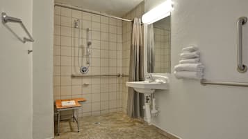 A small, clean bathroom with a sink, mirror, and handrails.