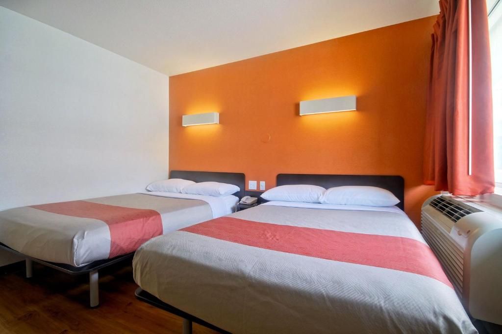 A hotel room with two beds, a wall-mounted phone, and an air conditioning unit.