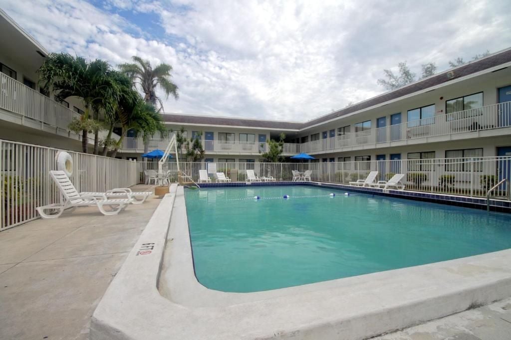 Piscina com espreguiçadeiras e guarda-sóis, rodeada por um edifício com vários andares e varandas.
