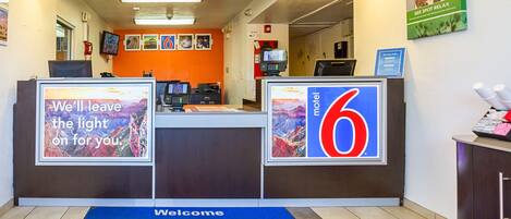 A motel lobby with a reception desk, a blue welcome mat, and a sign indicating the motel number.