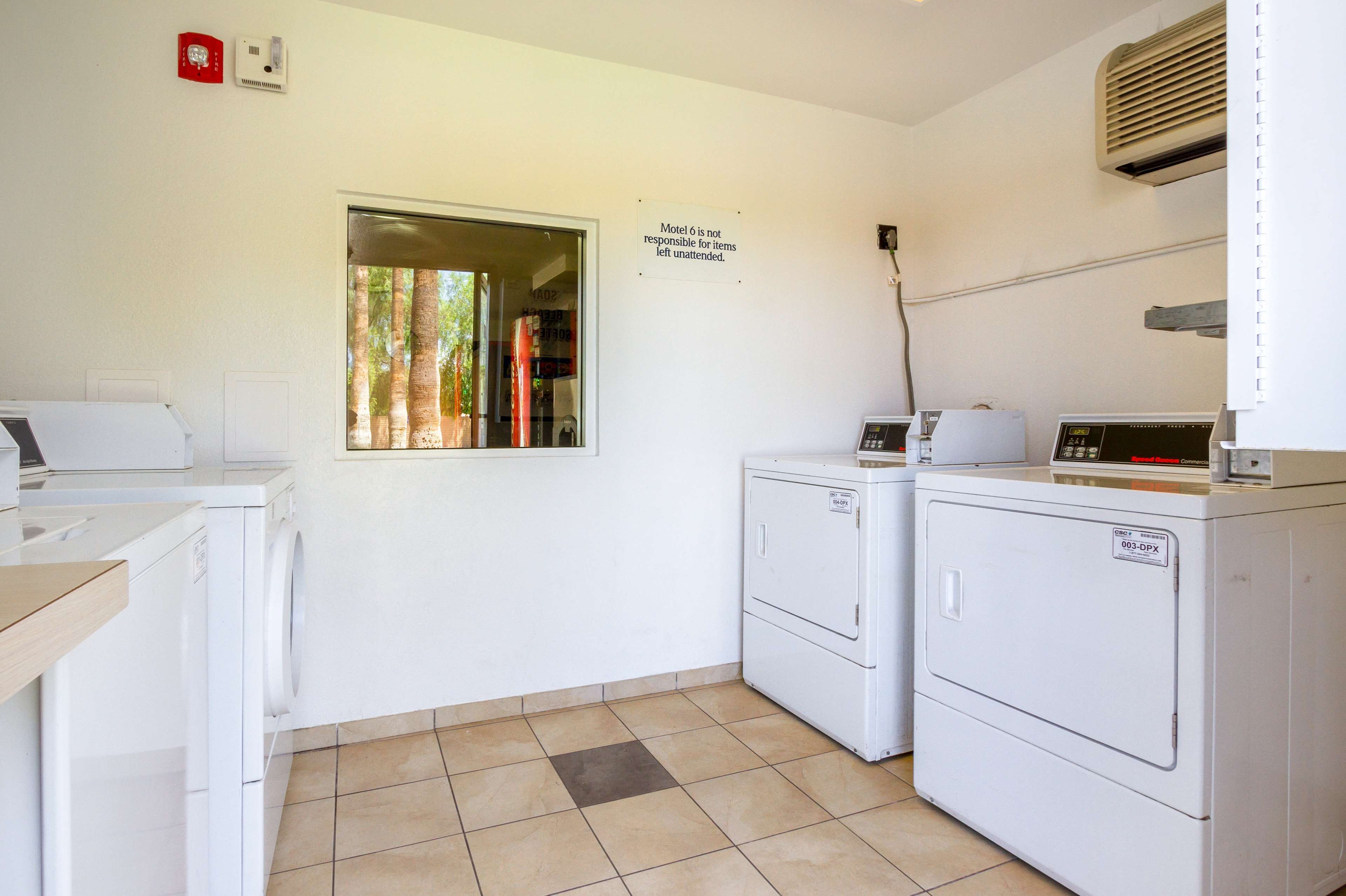 A laundry room with two front-loading washing machines, a dryer, and a window with a view of trees.