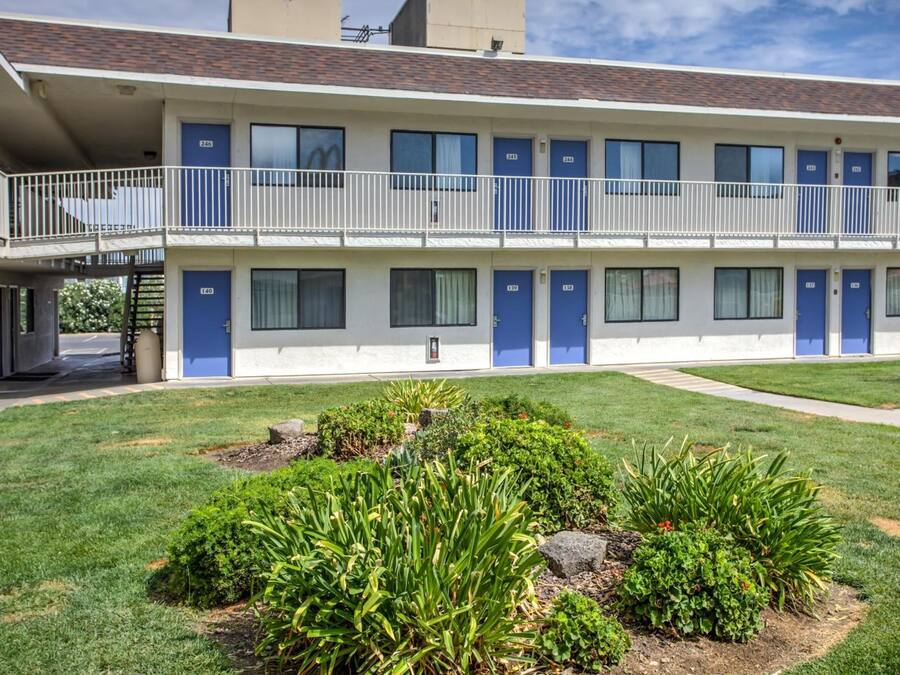 A two-story motel with a flat roof, multiple rooms, and a small garden area.