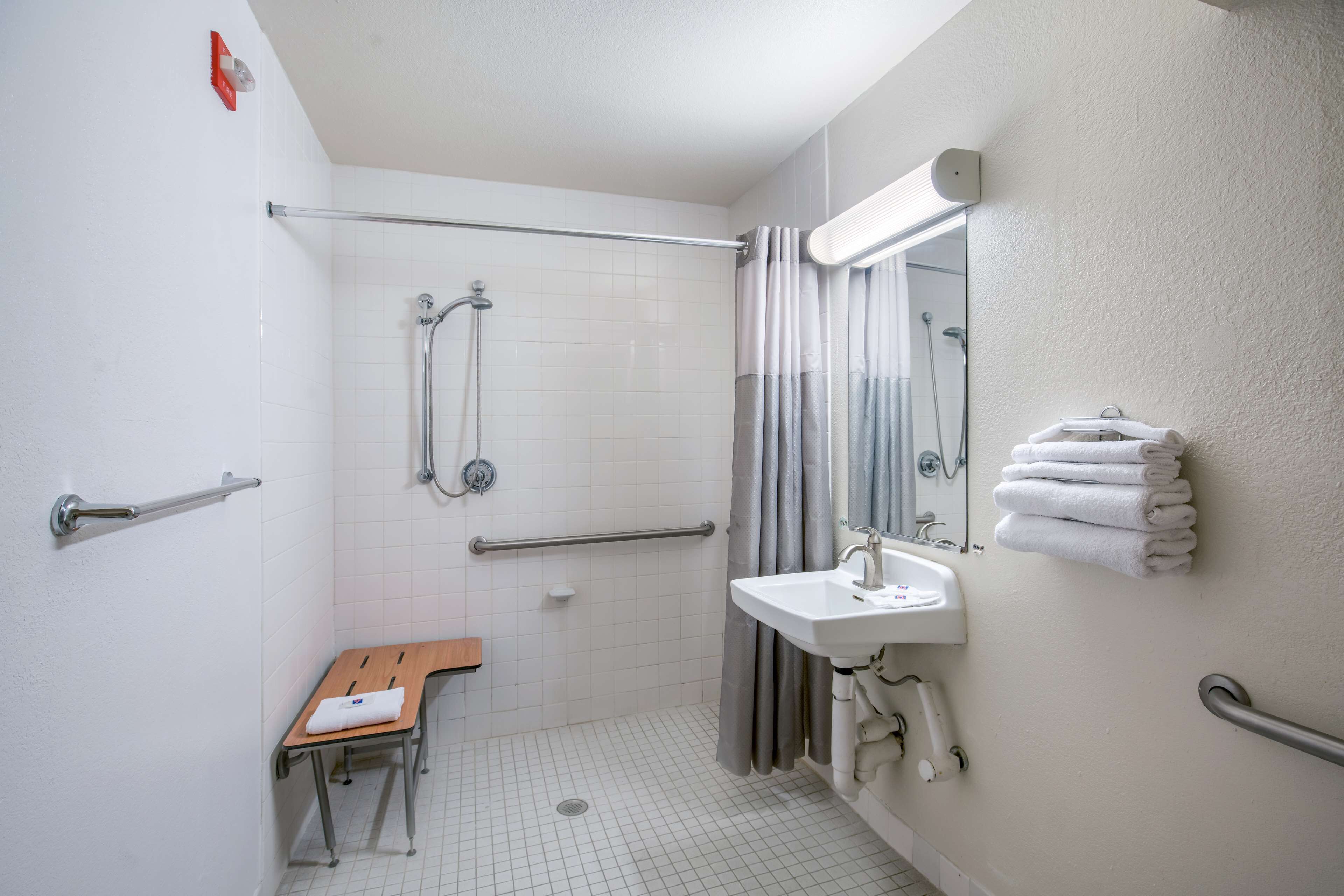 A bathroom with a shower, grab bars, a sink, and a toilet.