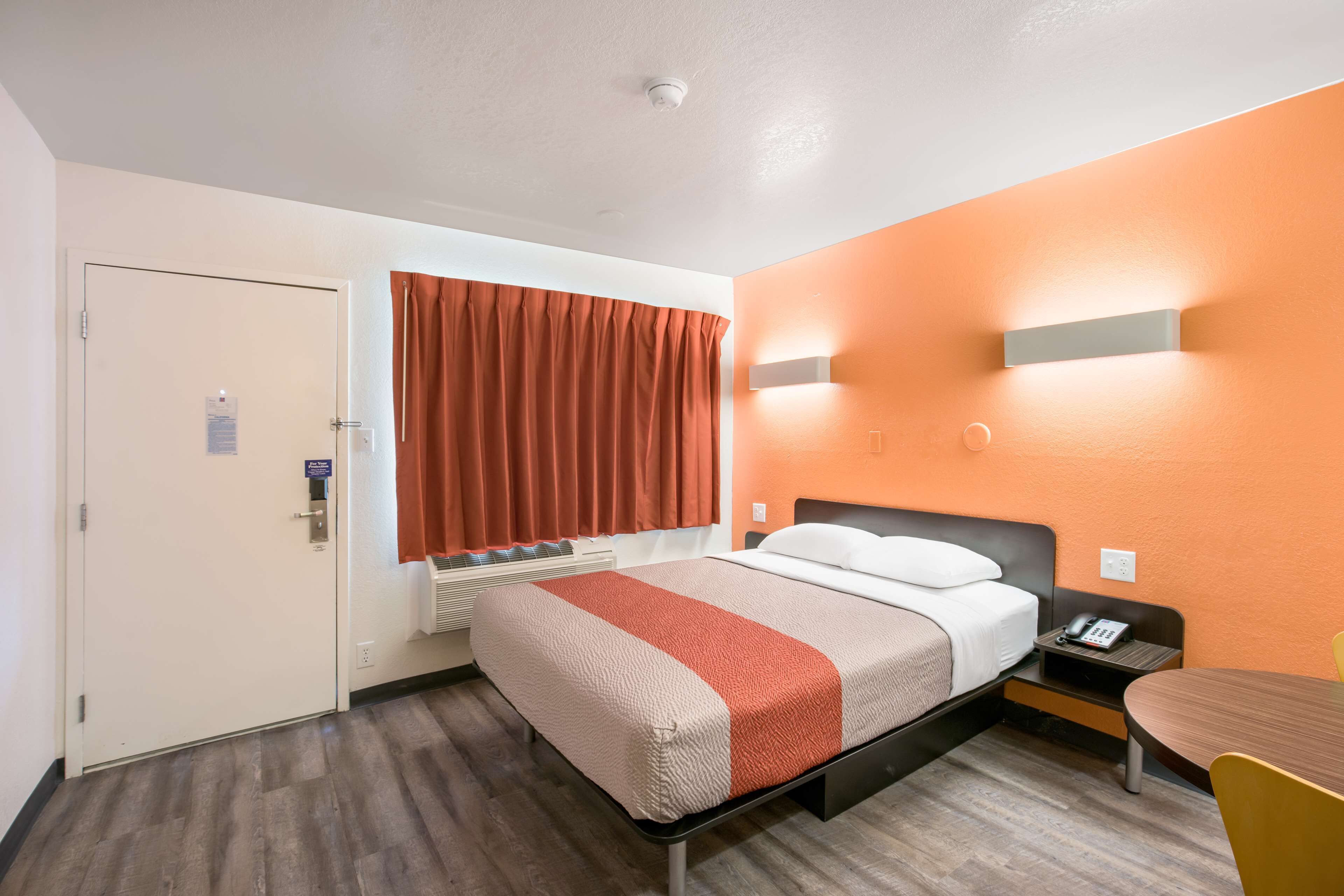 A hotel room with a bed, a nightstand, a chair, and a window with curtains.