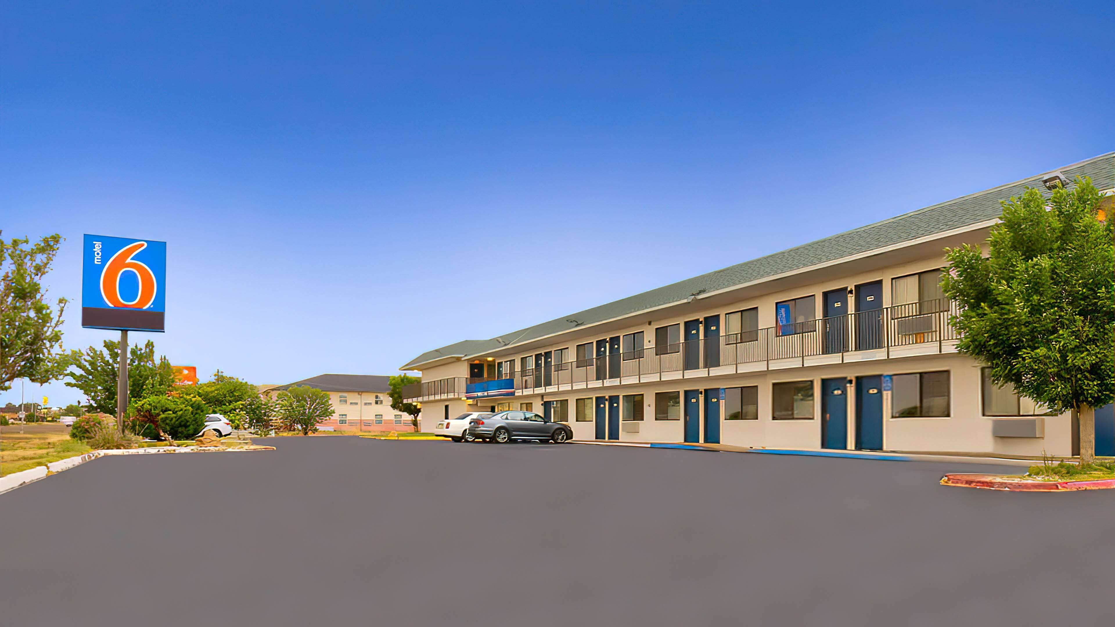 A motel with a large sign indicating 6 rooms. It features a two-story building with a flat roof and a parking lot in front.