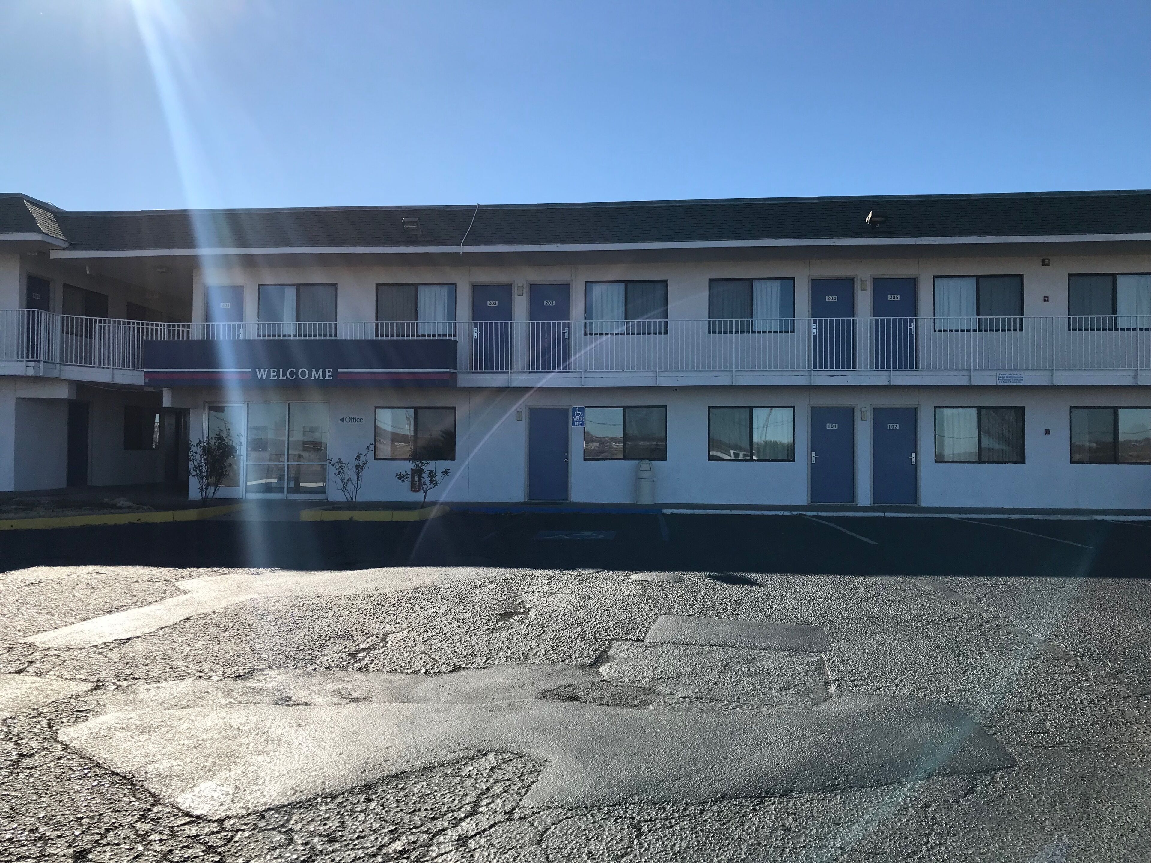 Um motel de dois andares com um letreiro de 'Welcome', quartos numerados e um estacionamento.