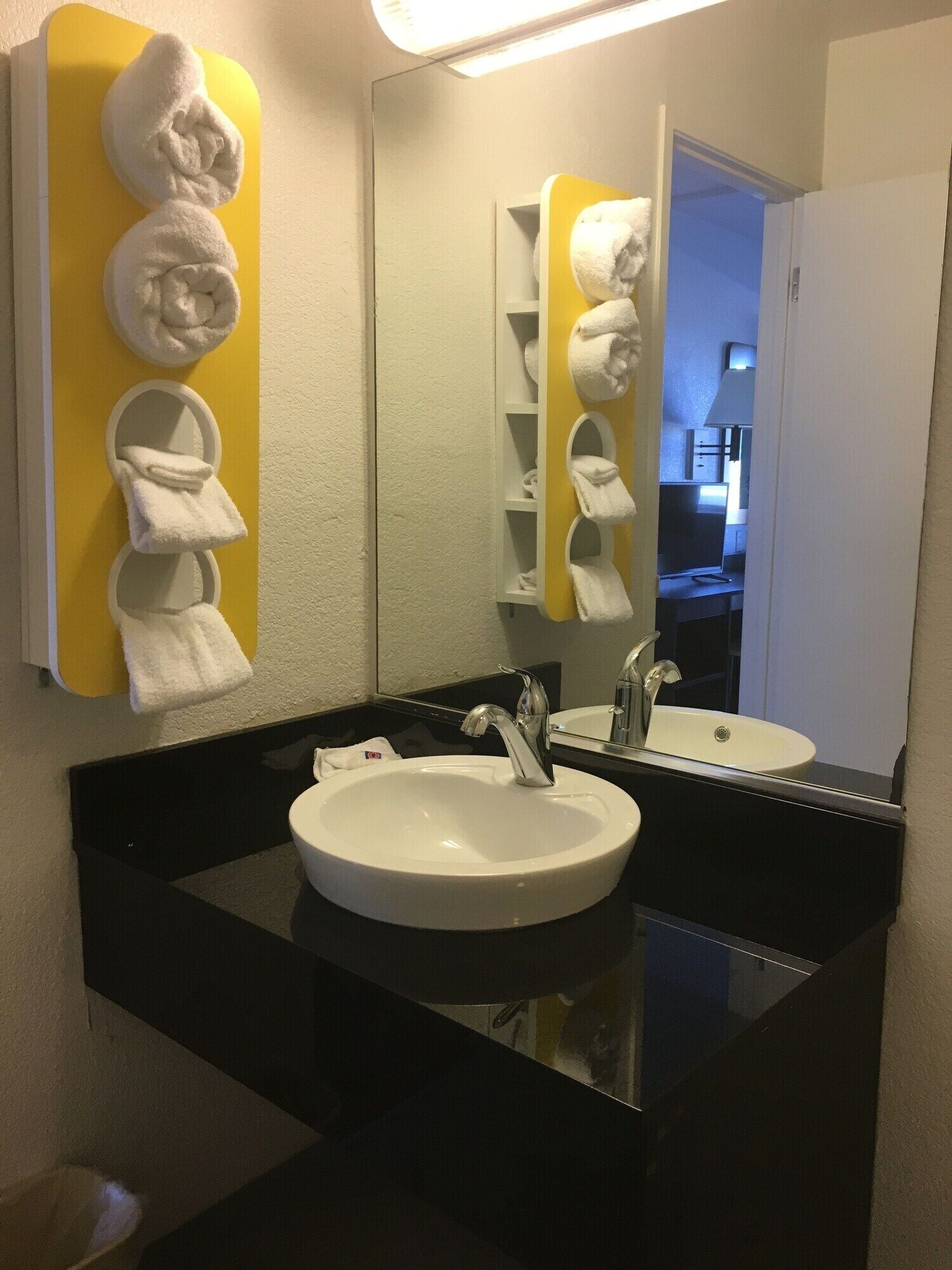 A bathroom with a white sink, two faucets, and a mirror. There are towel racks on the wall and a yellow towel holder.