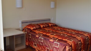 A single bed with a patterned blanket, a bedside table, and two wall-mounted light fixtures. - Super 7 Inn (Bossier City)