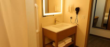 Un baño con lavamanos, espejo, toallero y ducha.