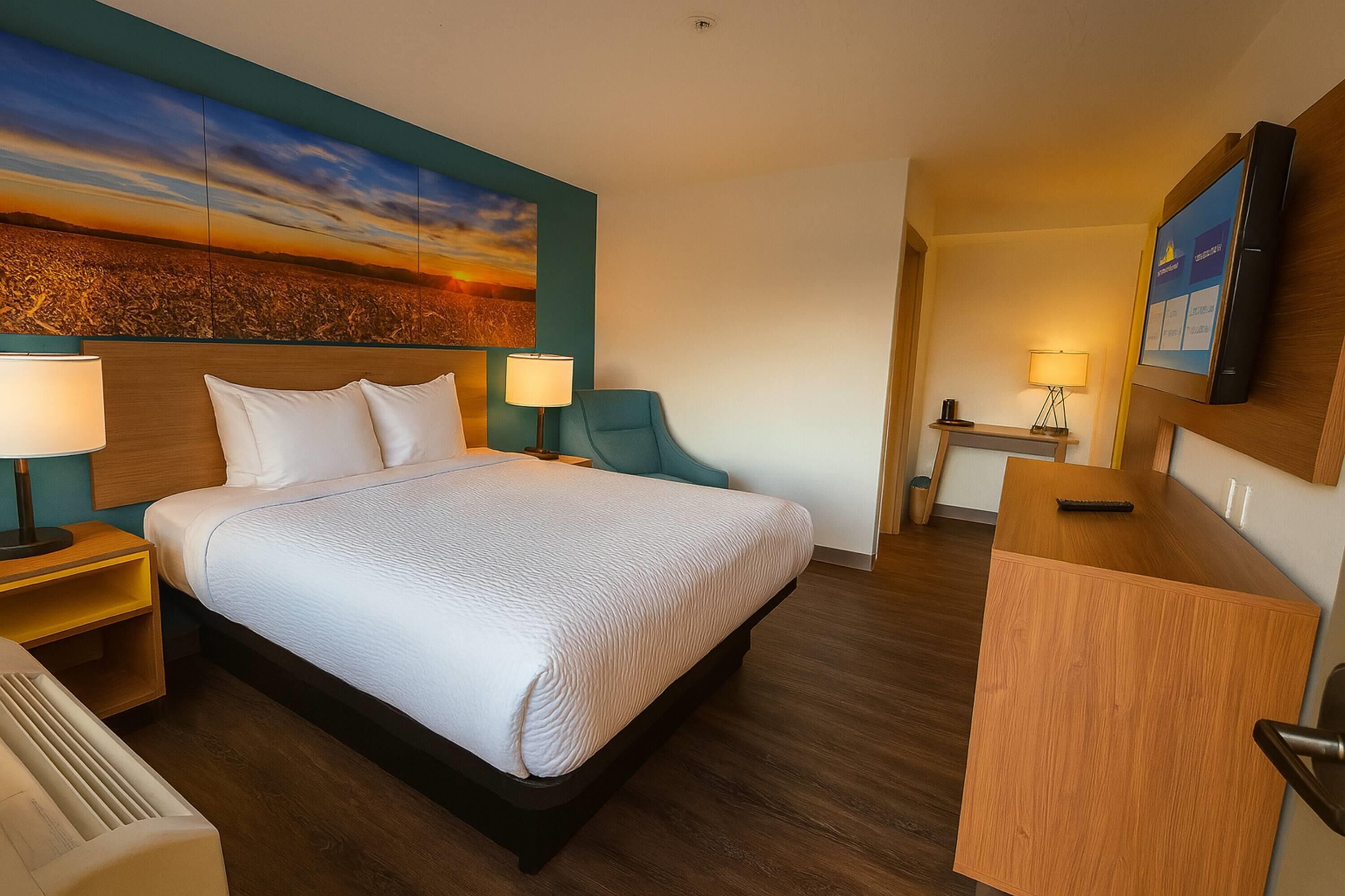 Una habitación de hotel con una cama grande, dos mesitas de noche con lámparas, un escritorio con una silla y un cuadro grande en la pared.