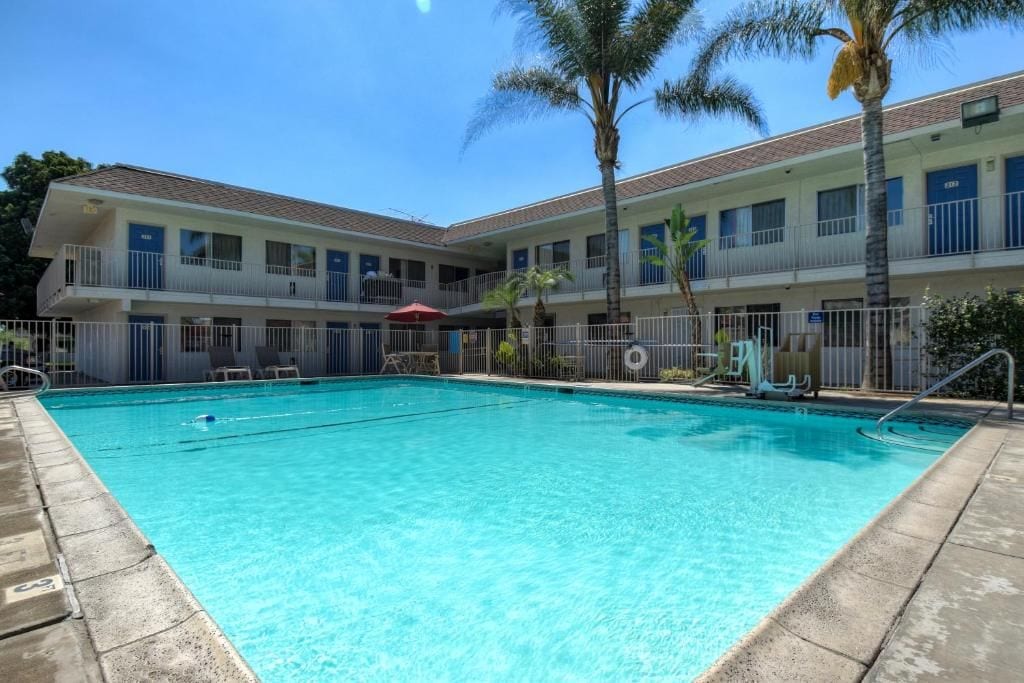 A hotel with a swimming pool, multiple balconies, and palm trees.