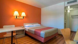 A hotel room with a bed, a desk, a chair, and a wall-mounted lamp. - Motel 6 Riverside West - Jurupa Valley (Jurupa Valley)