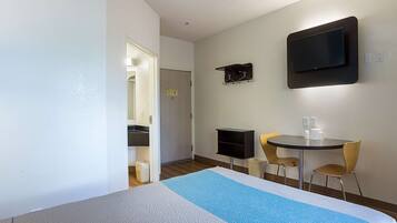 A hotel room with a bed, a TV mounted on the wall, a small table with chairs, and a trash bin.