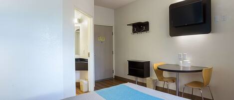 A hotel room with a bed, a TV mounted on the wall, a small table with chairs, and a trash bin.