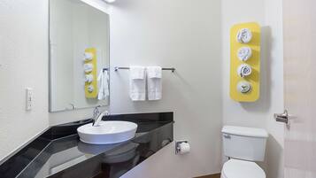 Un baño con lavamanos, espejo, toallero, inodoro y dispensador de toallas amarillo.