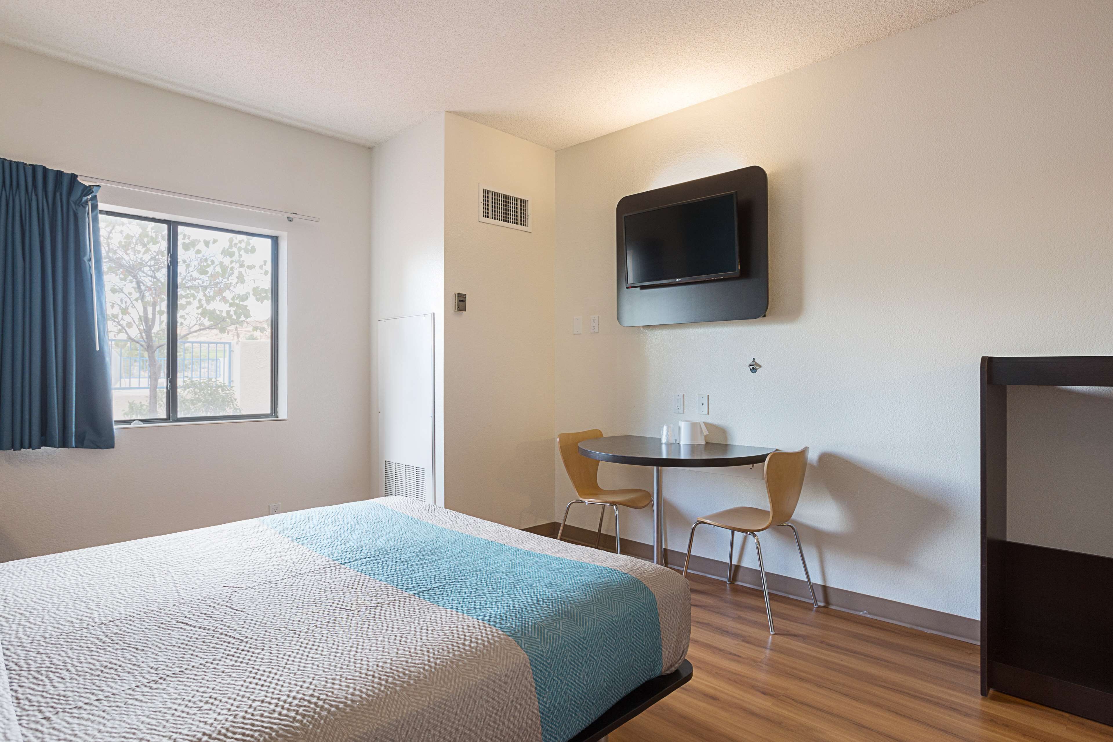 A hotel room with a bed, a desk, two chairs, a television, and a window with curtains.
