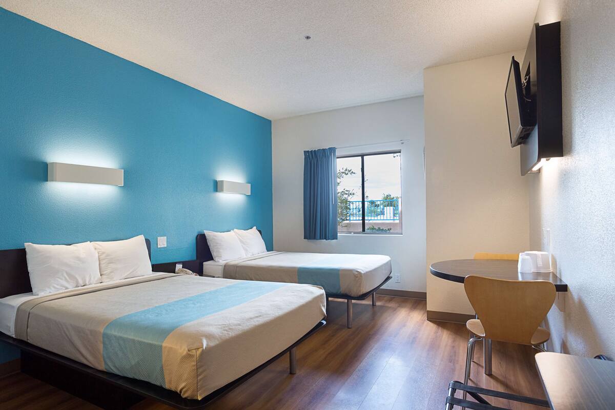 A hotel room with two beds, a small table, and a chair.