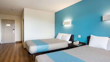 A hotel room with two beds, a wooden floor, a blue accent wall, and a bedside table with a phone.