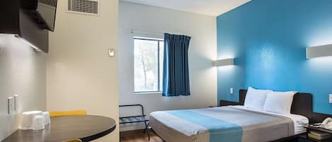 Una habitación de hotel con cama, mesita de noche y ventana con cortinas.