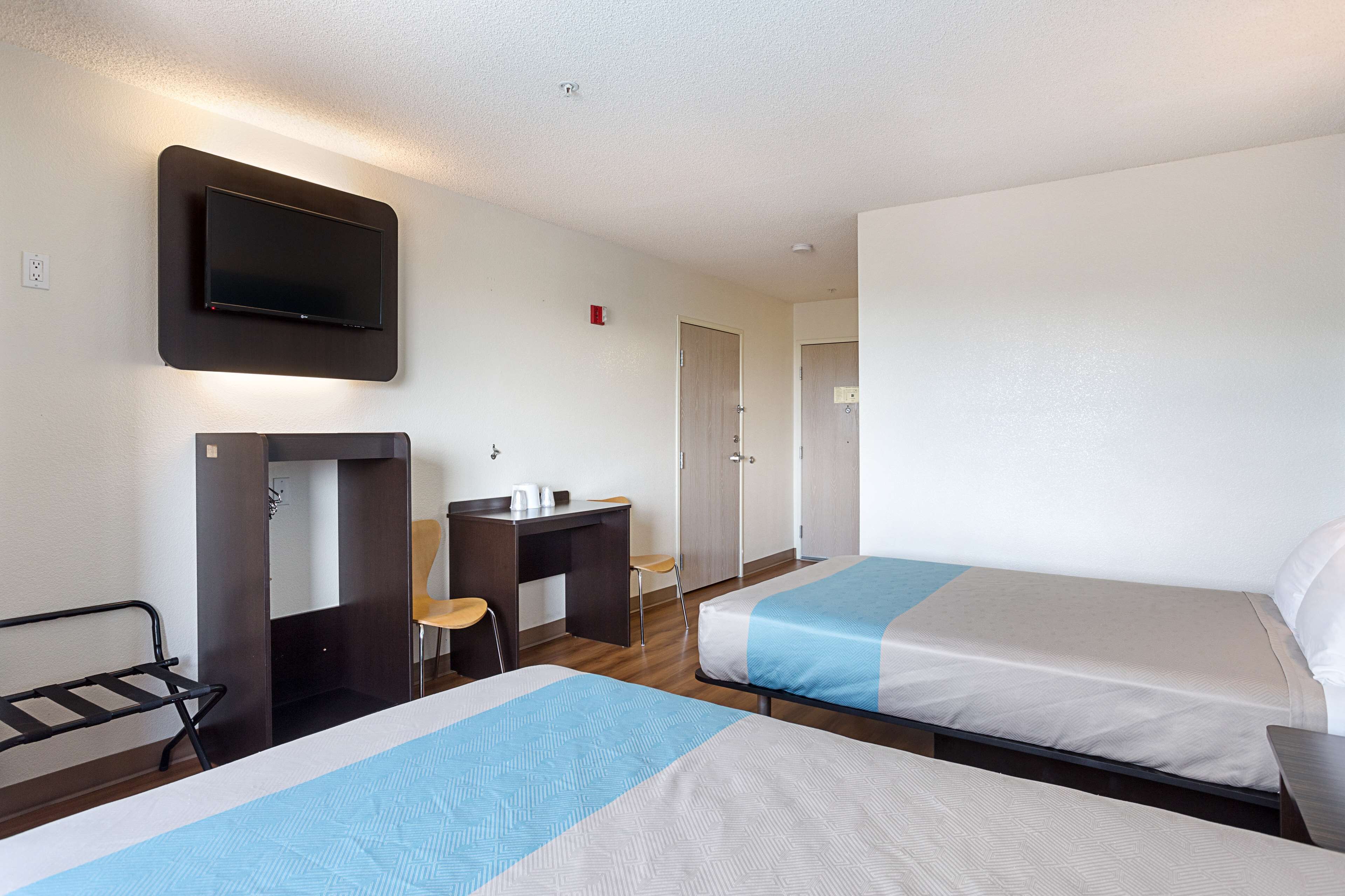 Une chambre d’hôtel avec deux lits, un bureau, une chaise, un téléviseur fixé au mur et une petite salle de bain.