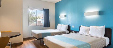 Habitación de hotel con dos camas, una mesa de comedor y una ventana con cortinas.