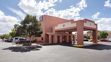 Un hotel con fachada roja, un acceso cubierto y un estacionamiento con varios coches.