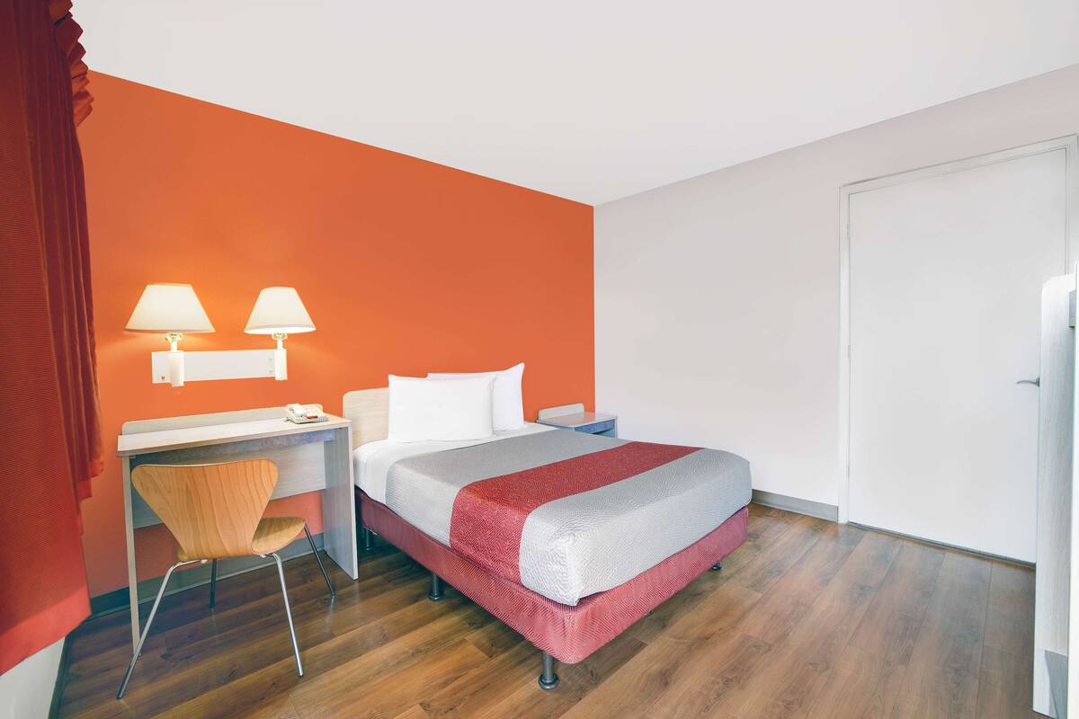 A hotel room with a bed, desk, chair, and two bedside lamps.
