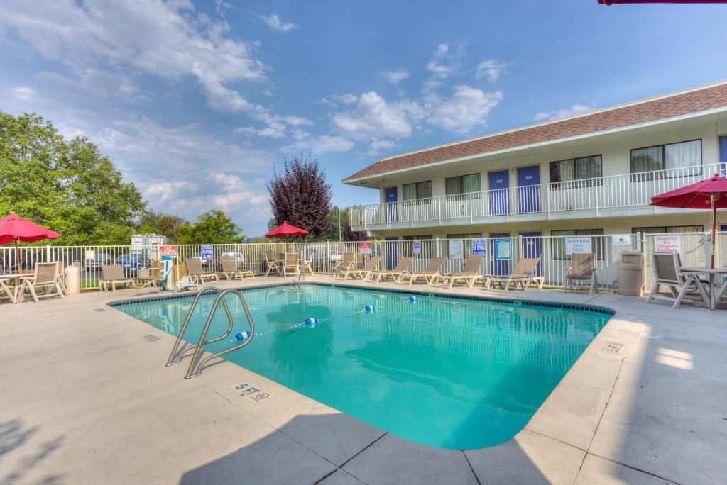 A pool area with lounge chairs and umbrellas, a building with multiple floors and balconies, and a clear sky.