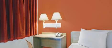 A hotel room with a bed, a desk with a lamp, a chair, and a telephone.