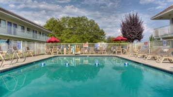 A swimming pool with lounge chairs and umbrellas, surrounded by a fence.