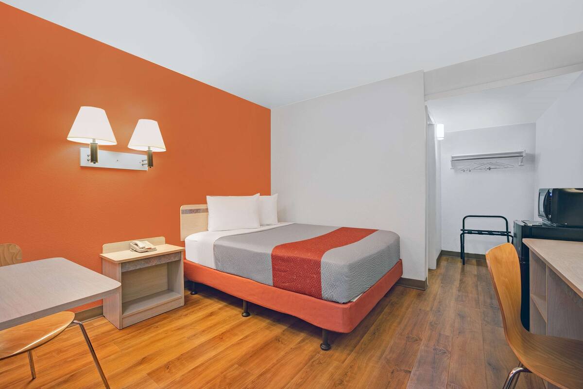 A hotel room with a bed, a desk, a chair, a TV, and a lamp.