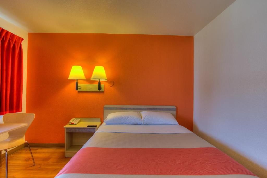 Habitación de hotel con cama, dos lámparas de noche, una mesita, una silla y una cortina roja.