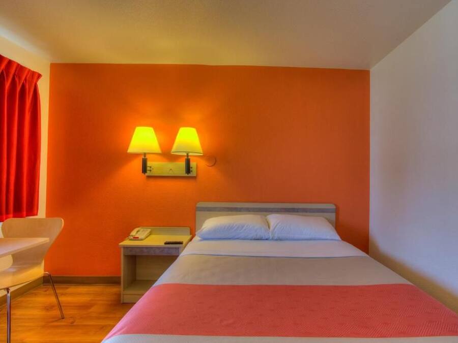 Habitación de hotel con cama, dos lámparas de noche, una mesita, una silla y una cortina roja.