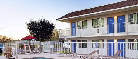 A hotel with a swimming pool, lounge chairs, and a red umbrella.